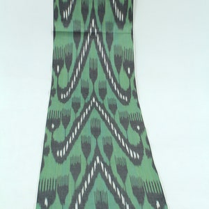 Può includere: Tessuto verde e nero con un motivo ripetitivo di fiori stilizzati. Il tessuto ha una leggera lucentezza e una texture morbida.