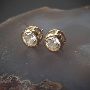 May include: A pair of gold stud earrings with clear round gemstones.