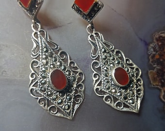 May include: A pair of silver earrings featuring a red carnelian stone and marcasite accents. The earrings are in a teardrop shape with a filigree design.