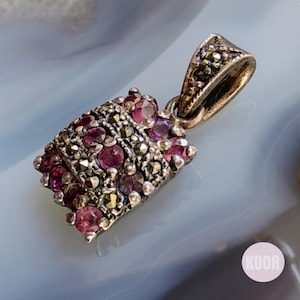 May include: A silver pendant with a rectangular shape, adorned with small pink gemstones and black marcasite stones.