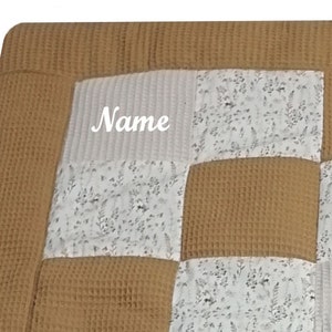 Könnte beinhalten: Eine beige Waffel-Babydecke mit Patchwork-Design. Die Decke hat ein weißes Quadrat mit dem Wort "Name" in der Mitte. Die Decke ist aus weichem, bequemem Stoff und perfekt zum Kuscheln.
