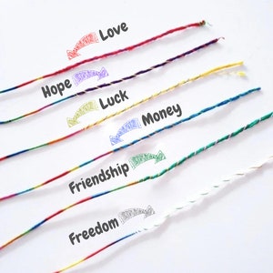 Può includere: Primo piano di braccialetti dell'amicizia colorati con le parole "Amore", "Speranza", "Fortuna", "Denaro", "Amicizia" e "Libertà" scritte sopra. I braccialetti sono fatti di fili intrecciati in vari colori, tra cui rosso, viola, giallo, blu, verde e bianco.