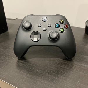 May include: Black Xbox controller with colored buttons, including green A, red B, blue X, and yellow Y. The controller has two analog sticks, a directional pad, and several other buttons. The Xbox logo is visible at the top.