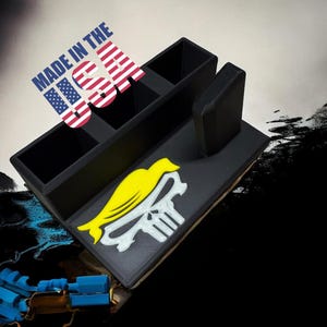 May include: Black desk organizer with multiple compartments and a yellow bird and skull emblem. The phrase "MADE IN THE USA" is printed on a sticker above the organizer.