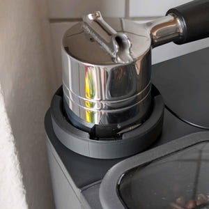 May include: A close-up of a chrome espresso machine portafilter and tamper. The portafilter is attached to the machine, with a black handle. The tamper is chrome and cylindrical. The machine is black with a clear bean container.