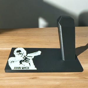 May include: Black plastic stand with a silhouette of John Wick holding a gun and the text "JOHN WICK" on the base.
