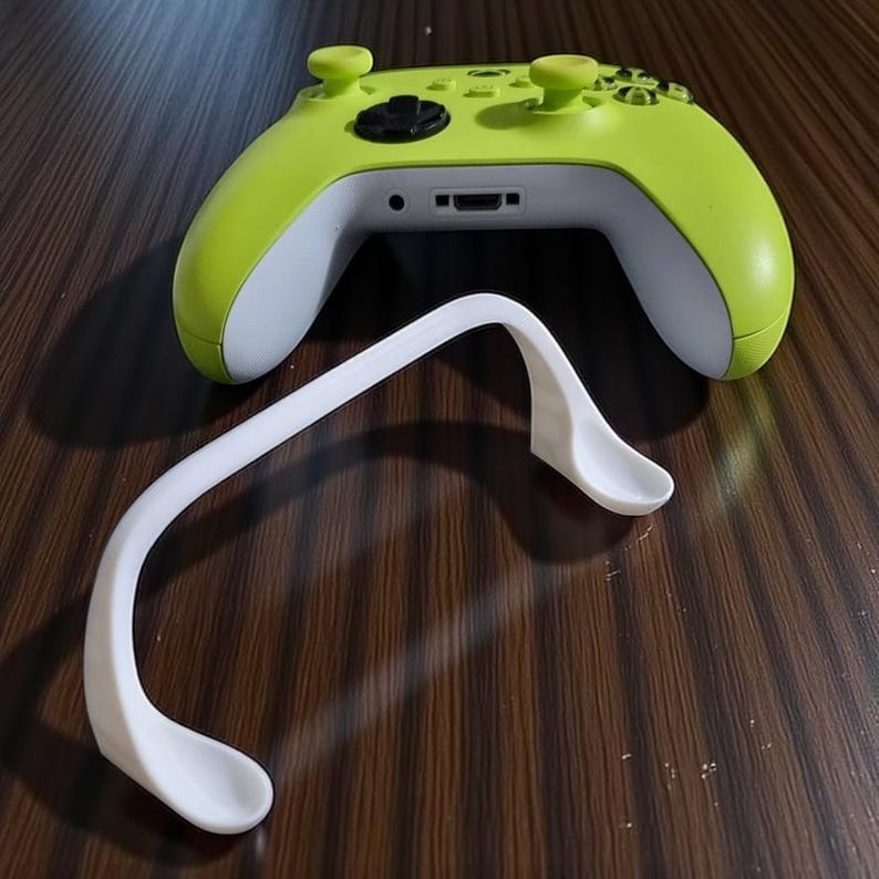 May include: A lime green and white video game controller with a white accessory. The controller has black buttons and green thumbsticks. The accessory is white and curved, with two spoon-like ends.