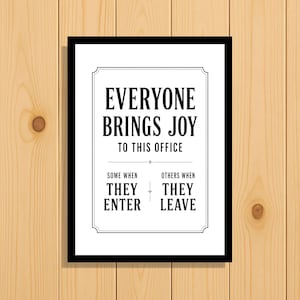 Op de afbeelding: Een rechthoekig wandbord met een zwarte lijst en een witte achtergrond met de zwarte tekst: EVERYONE BRINGS JOY TO THIS OFFICE. SOME WHEN THEY ENTER, OTHERS WHEN THEY LEAVE. De tekst is gecentreerd binnen een dunne zwarte decoratieve rand.