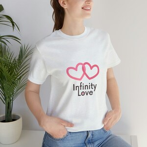 May include: White t-shirt with a pink infinity symbol made of two hearts and the text "Infinity Love" printed on the front.