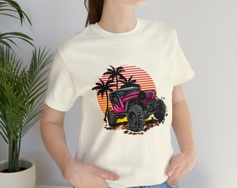 May include: White t-shirt featuring a pink jeep driving through a sunset scene with palm trees. The jeep has black wheels and a black roof.