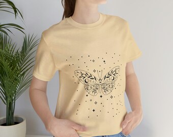May include: A light yellow t-shirt with a black butterfly design. The butterfly has a celestial theme with moons and stars. The shirt is decorated with a scattering of small stars.