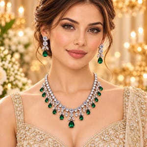 May include: A jewellery set consisting of a necklace and matching drop earrings. The necklace features a silver-toned metal chain adorned with clear round and marquise-cut stones, interspersed with vibrant green pear-shaped teardrop gemstones.