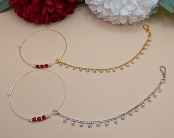 May include: Two gold and silver nose rings with red and white beads. The nose rings are on a light brown background.