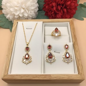 Peut inclure: Un ensemble de bijoux en or avec des pierres précieuses rouges en forme de poire et des accents de zircone cubique clairs. L'ensemble comprend un collier, une bague et une paire de boucles d'oreilles.
