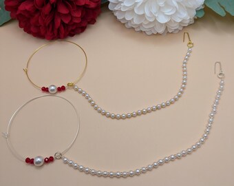 May include: Two gold nose rings with a pearl and red beads hanging from a chain of white pearls.