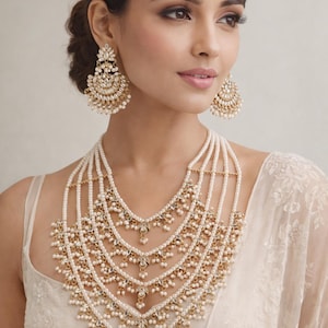 Peut inclure: Un ensemble de bijoux doré orné comprenant un collier de perles à plusieurs rangs, des boucles d'oreilles assorties et un serre-tête. Le collier présente un design superposé avec des détails dorés complexes et des perles. Les boucles d'oreilles et le serre-tête reprennent le design du collier.
