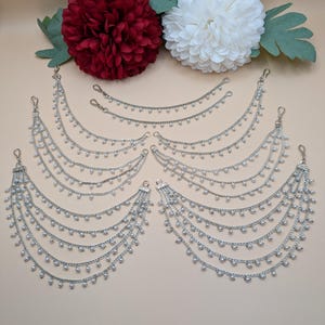 May include: A set of five pairs of silver hair chains with small pearl accents. Each chain has a hook on each end for attaching to hair.