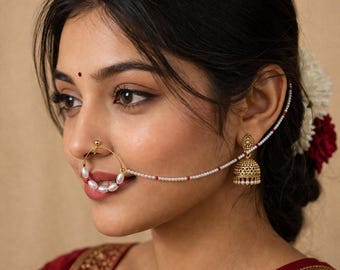 May include: A gold-toned nose ring with a pearl and bead chain, connected to a matching earring. The nose ring features a large hoop with white pearls. The earring has a bell shape with intricate detailing.