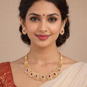 Peut inclure: Un collier doré et une paire de boucles d'oreilles assorties. Les bijoux présentent des pierres précieuses rouges ovales serties dans un motif floral. Le collier est composé de plusieurs grappes de pierres précieuses reliées par une chaîne perlée.