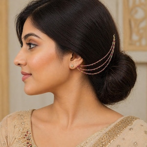 May include: A gold-toned ear cuff with three delicate chains adorned with small, red gemstones. The ear cuff is attached to a small stud earring. The jewelry is worn on the ear.