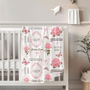 May include: A white baby blanket with a pink floral pattern and the name "Gemma Grace" repeated throughout. The blanket also features butterflies and ornate frames.