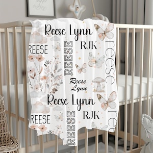 May include: White baby blanket with a floral and butterfly design. The blanket features the names "Reese Lynn" and "RJK" repeated throughout the design.
