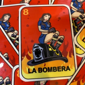 May include: A red and yellow card with a woman in a blue shirt and black boots sitting on a black firefighter's helmet. The card has the number 8 and the text "LA BOMBERA" on it.