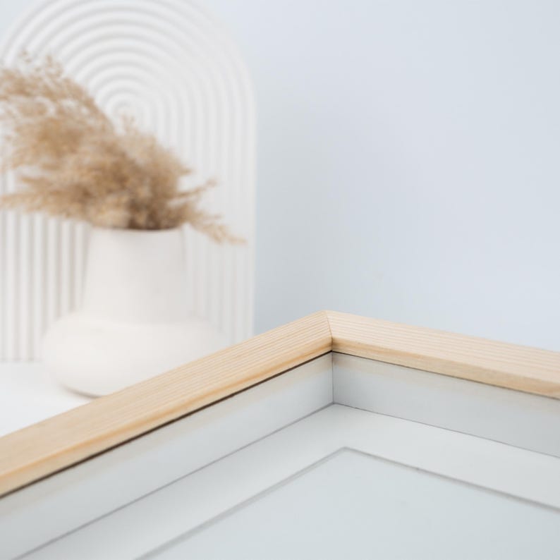 May include: Close-up of the top corner of a light wood picture frame with a white mat. The frame is sitting on a white surface.