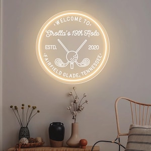 May include: A circular neon sign with a warm white glow featuring the text "WELCOME TO, Strolla's 19th Hole, ESTD, 2020, FAIRFIELD GLADE, TENNESSEE" and a central graphic of two crossed golf clubs behind a golf ball on a tee.