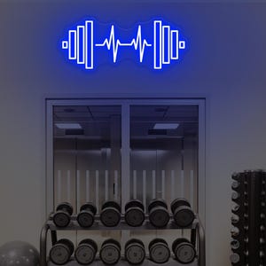 May include: A bright blue neon wall sign featuring a stylized graphic of a dumbbell with a central heartbeat EKG line. The design consists of vertical bars on each side of the pulse wave, creating a glowing, linear aesthetic on the wall.