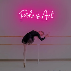 Può includere: Un'insegna al neon rosa con la scritta "Pole is Art" sopra una ballerina in body e tutù neri, che si allunga a una sbarra di danza classica. La ballerina indossa scarpe da punta. Lo sfondo è un muro rosa chiaro.
