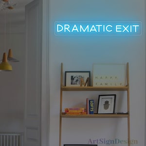 May include: A blue neon sign that reads "DRAMATIC EXIT" is mounted on a white wall. Below the sign is a wooden shelf with framed pictures, books, and decorative items. The room has a modern, minimalist design.