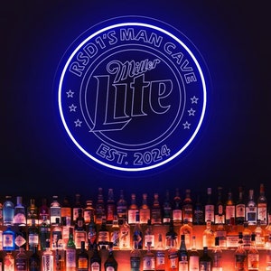 Pode incluir: Uma placa de néon azul com o texto "RSD1's Man Cave Miller Lite EST. 2024" acima de um bar. O bar está abastecido com garrafas de licor e artigos de vidro, com uma frente de madeira e prateleiras.