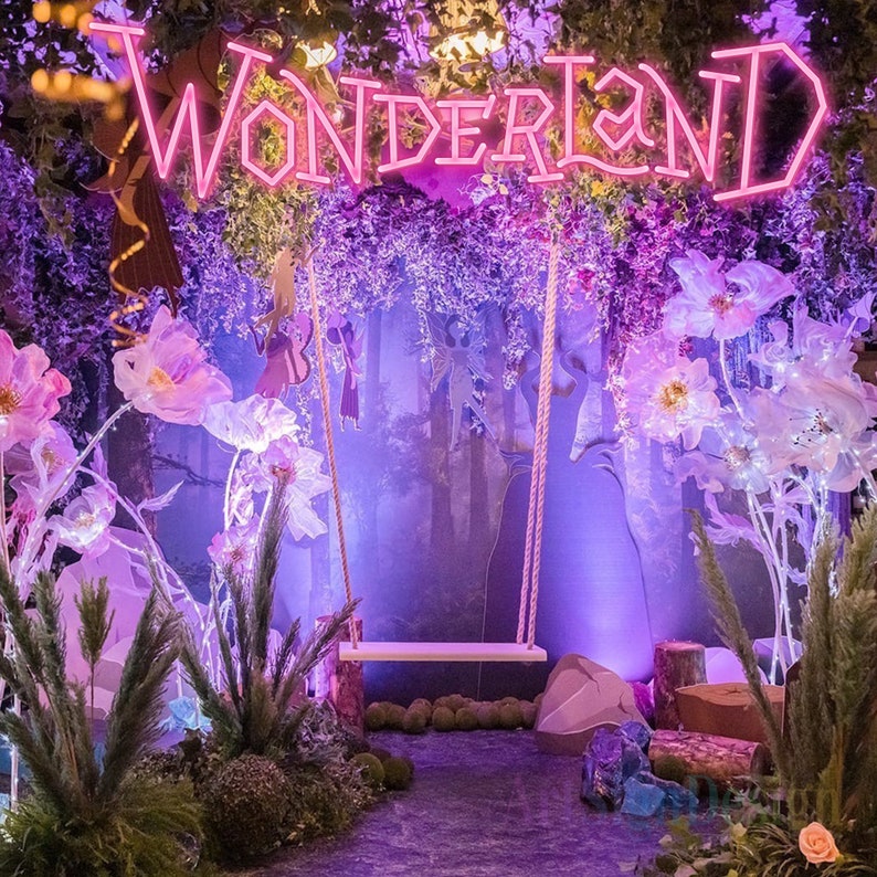 May include: A whimsical wonderland scene with a neon sign that reads "WONDERLAND" and a white swing hanging from a purple floral backdrop. The scene is decorated with large, white paper flowers and a purple, leafy forest.