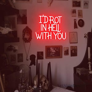 May include: A red neon sign displaying the text "I'D ROT IN HELL WITH YOU". The sign is set against a wall adorned with framed pictures and gothic-style decorative elements.