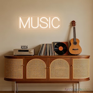 Peut inclure: Une enseigne néon murale affichant le mot MUSIC en lettres capitales blanches lumineuses avec une bordure ondulée. L'enseigne est placée au-dessus d'un buffet en bois doté de quatre portes en cannage, d'un lecteur de cassettes, de vinyles et d'un ukulélé.