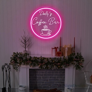 May include: A pink neon sign with a white outline that reads "Dolly's Coffee Bar" with a stylized coffee cup image below the text. The sign is hanging on a white wall above a fireplace mantel decorated with a green garland.