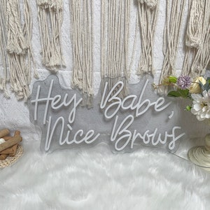 May include: White neon sign with the text "Hey Babe, Nice Brows" on a clear acrylic background.