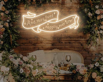 May include: A neon sign with the words "And they lived happily ever after" in a banner design. The sign is surrounded by floral arrangements and set against a wooden backdrop, creating a romantic ambiance.