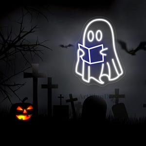 Op de afbeelding: Een wit neon-bord met een geest die een boek leest in een kerkhof. De geest is wit omrand met twee zwarte ogen en een blauw boek. De achtergrond is een donker silhouet van een kerkhof met een jack-o-lantern op de voorgrond.