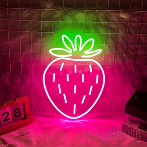 May include: A pink neon sign shaped like a strawberry with a green stem and leaves. The sign is lit up and glowing.
