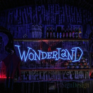 May include: A neon sign with the word "WONDERLAND" in a blue neon font. The sign is mounted on a dark wall with a wooden shelf above it. The shelf is filled with bottles of alcohol.