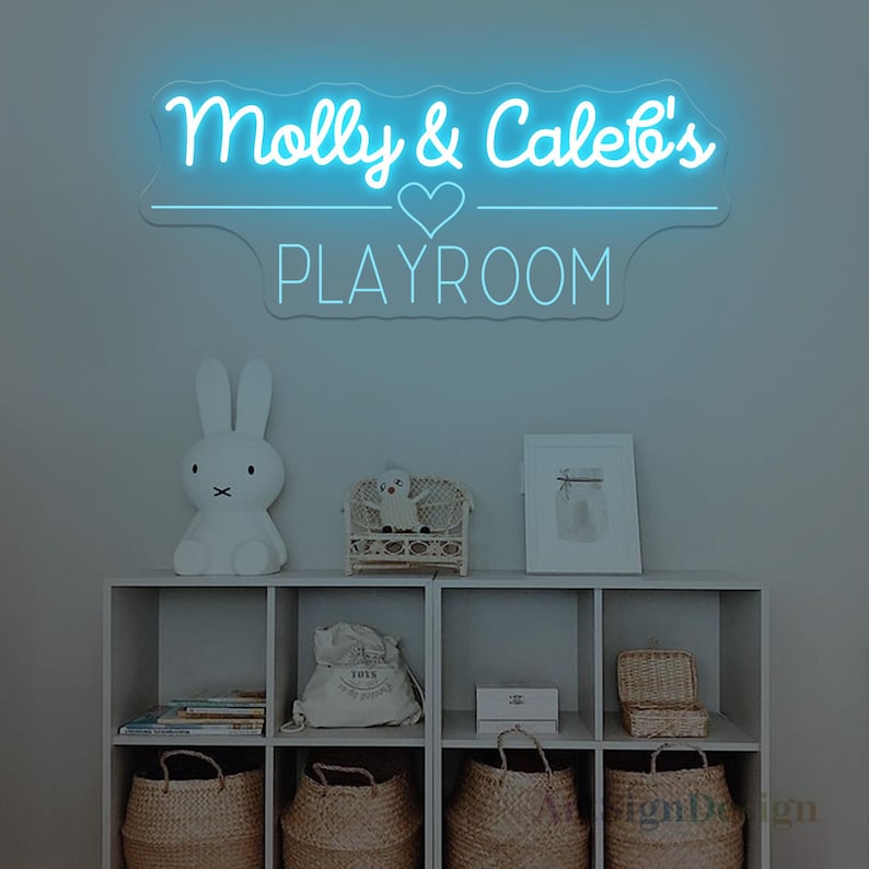 May include: A neon sign in light blue illuminates the words "Molly & Caleb's PLAYROOM" above a shelf. The shelf displays a white bunny lamp, a small wicker chair with a doll, a framed picture, and woven baskets. The sign is a decorative element for a playroom.