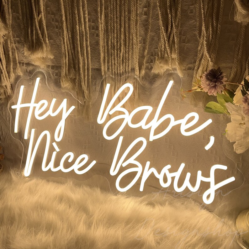 May include: White neon sign with the text "Hey Babe, Nice Brows" in a cursive font.
