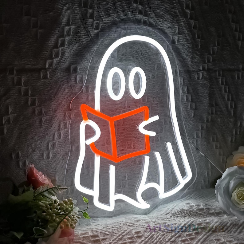 Op de afbeelding: Een wit neon-bord met een geest die een boek leest. De geest heeft twee grote ogen en een boek met een oranje gloed. Het bord is op een donkere achtergrond.