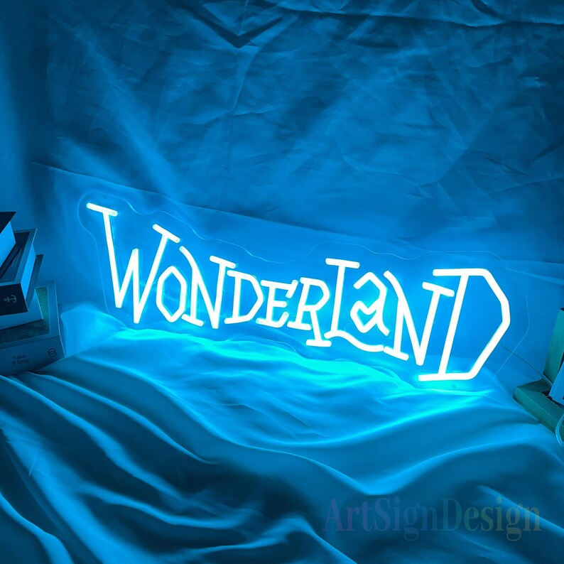 May include: White neon sign with the word "WONDERLAND" in a stylized font. The sign is lit up with a blue glow and is on a blue fabric background.