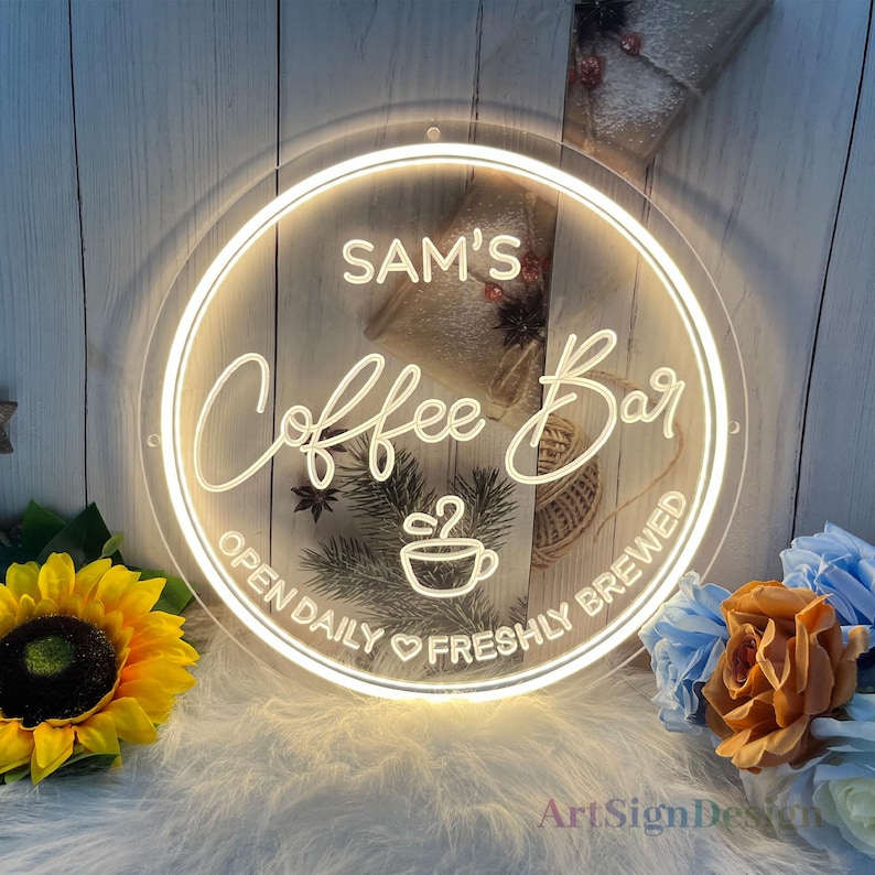 May include: A white neon sign with a round, clear frame. The sign says "Sam's Coffee Bar" with a coffee cup icon and the text "Open Daily &hearts; Freshly Brewed".
