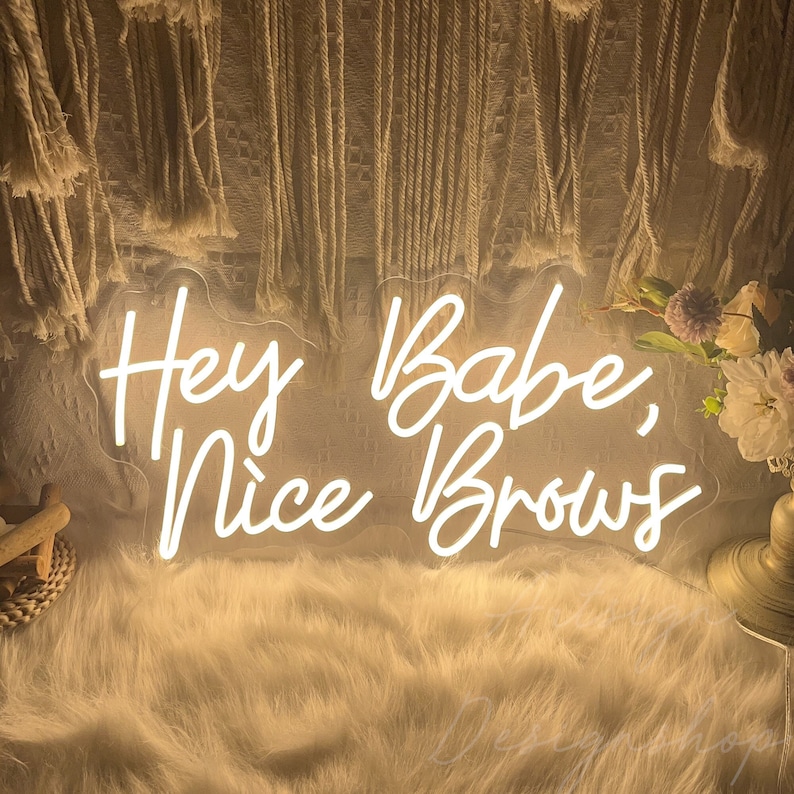 May include: White neon sign with the text "Hey Babe, Nice Brows" on a white background.