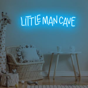 Op de afbeelding: Een felblauw neonbord aan een muur met de tekst "LITTLE MAN CAVE" in een informeel, handgeschreven lettertype. Het bord straalt een zacht, gloeiend licht uit en vormt een duidelijk visueel middelpunt tegen de muur.