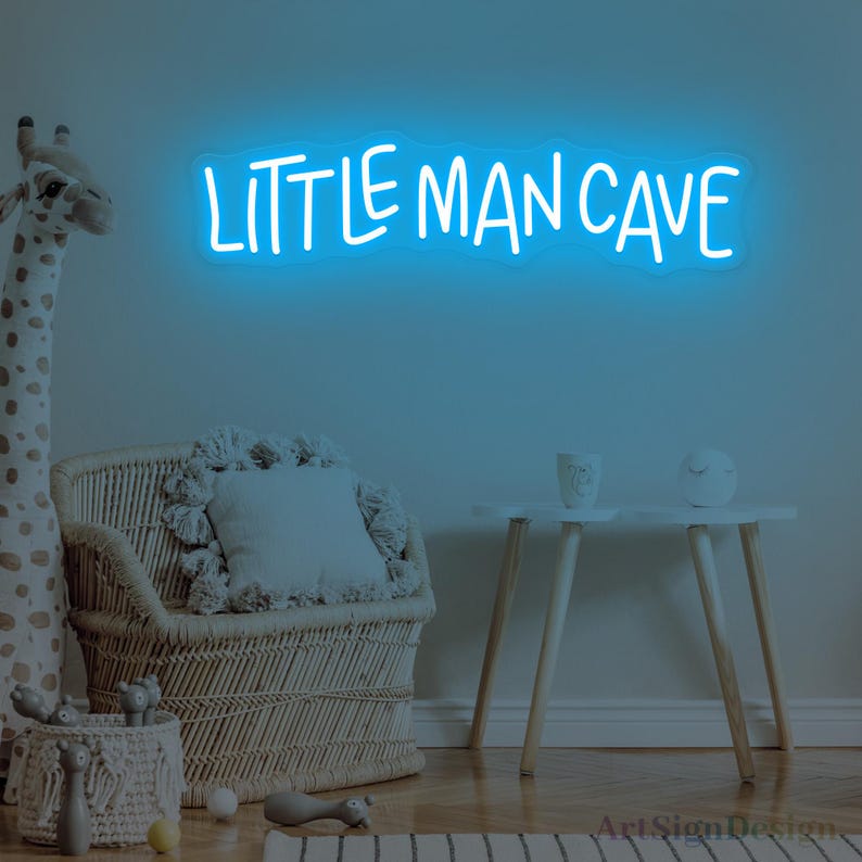 Op de afbeelding: Een felblauw neonbord aan een muur met de tekst "LITTLE MAN CAVE" in een informeel, handgeschreven lettertype. Het bord straalt een zacht, gloeiend licht uit en vormt een duidelijk visueel middelpunt tegen de muur.